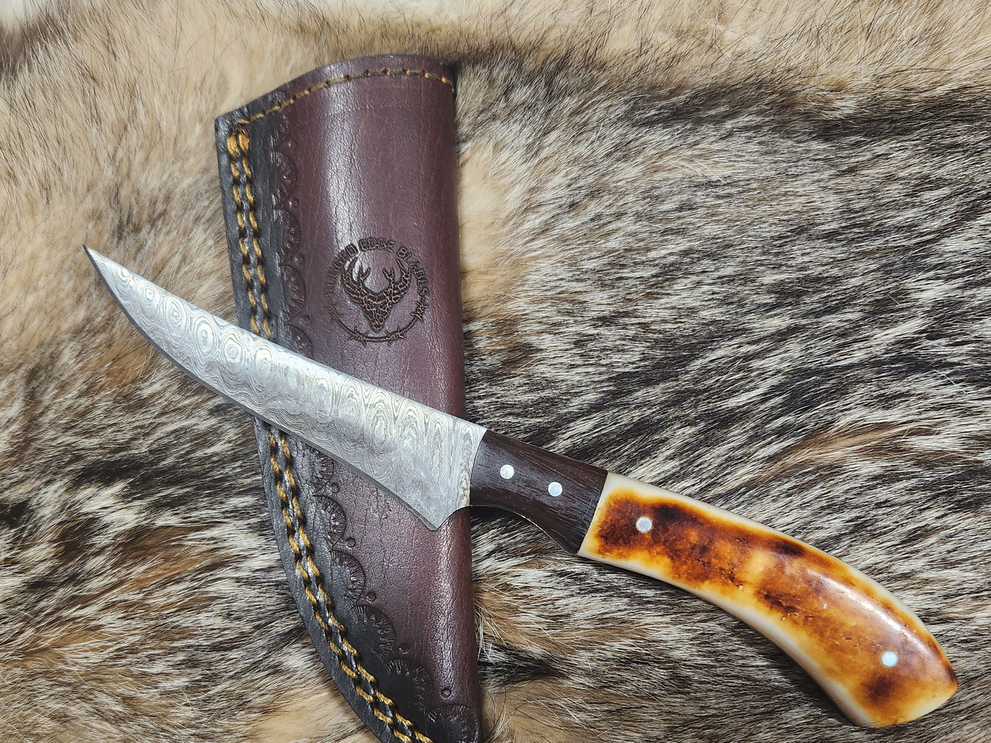 Small Bone Filet knife with Damascus steel blade and polished bone handle, displayed on fur with embossed leather sheath. Ideal for precision filleting.