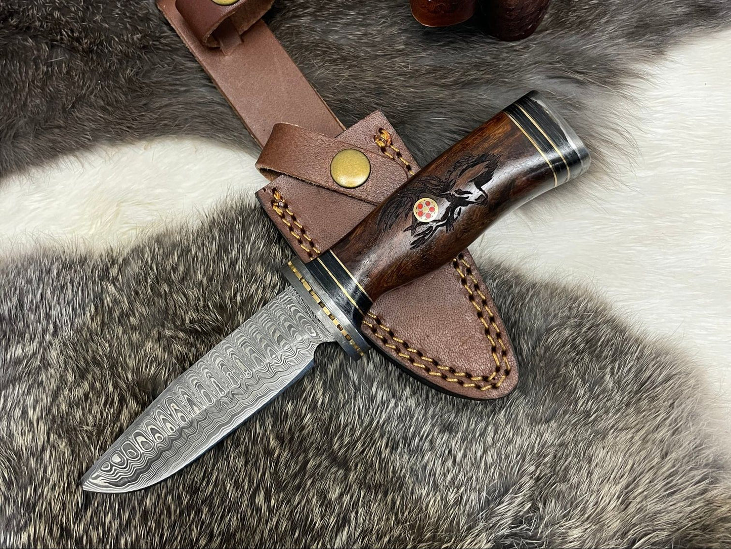 Eldertree Damascus steel hunting knife with engraved blade and polished wooden handle, displayed with leather sheath on fur background. Ideal for camping and survival use.