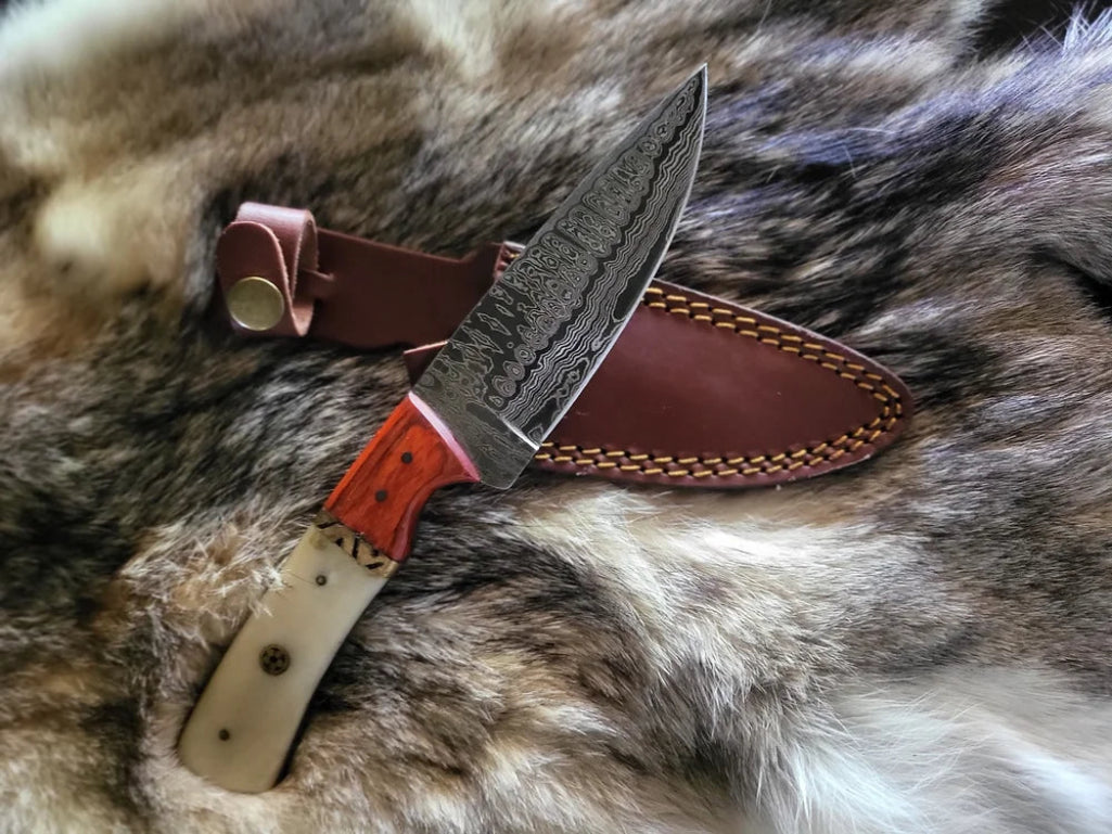A Damascus steel hunting and utility knife with a brown and black handle, a polished metal finish, and a sheath attached.