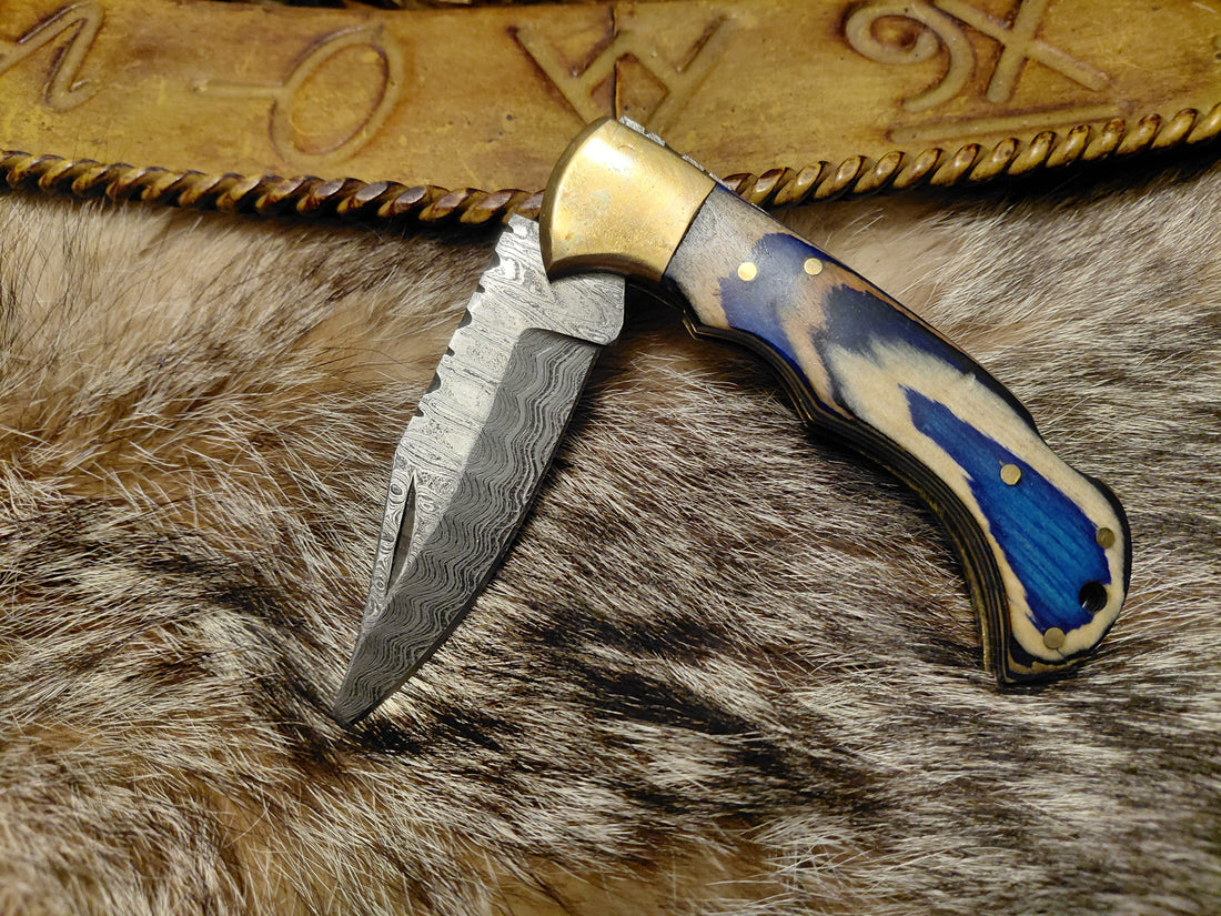 The Blue Wave Folding Knife from Rugged Edge Blades laying on an animal pelt, under a stamped leather belt.