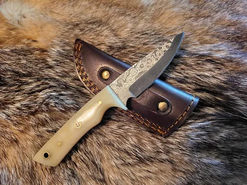 This bone handle EDC knife is laying on top of it's matching leather sheath over an animal pelt.