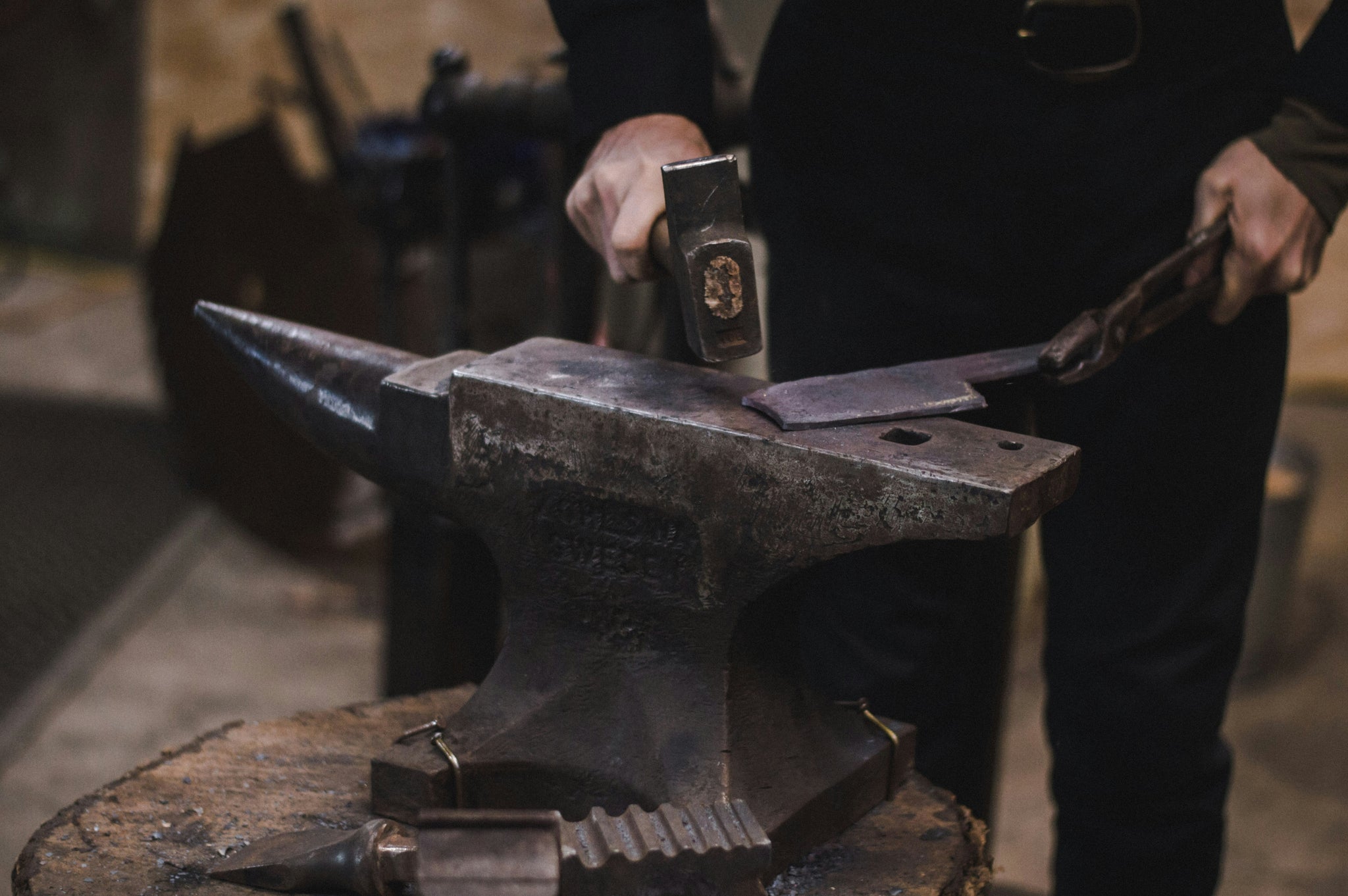 A bladesmith using his hammer and anvil to refine the shape of a custom hand-made knife.