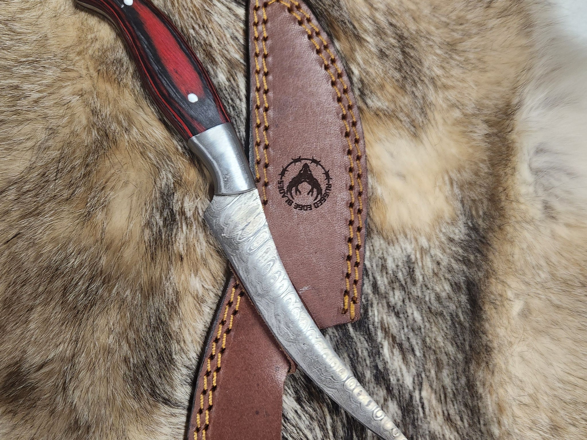 Small Red Filet knife with a curved Damascus steel blade and red wood handle, displayed on a leather sheath with fur background. Ideal for precision filleting.