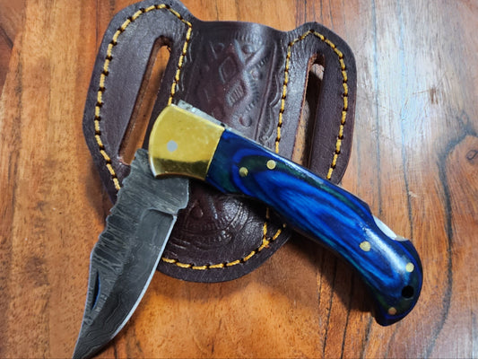Blue Diamond Wood Folder locking blade knife with Damascus steel blade and blue wood handle, displayed on a leather sheath for camping and hiking use.
