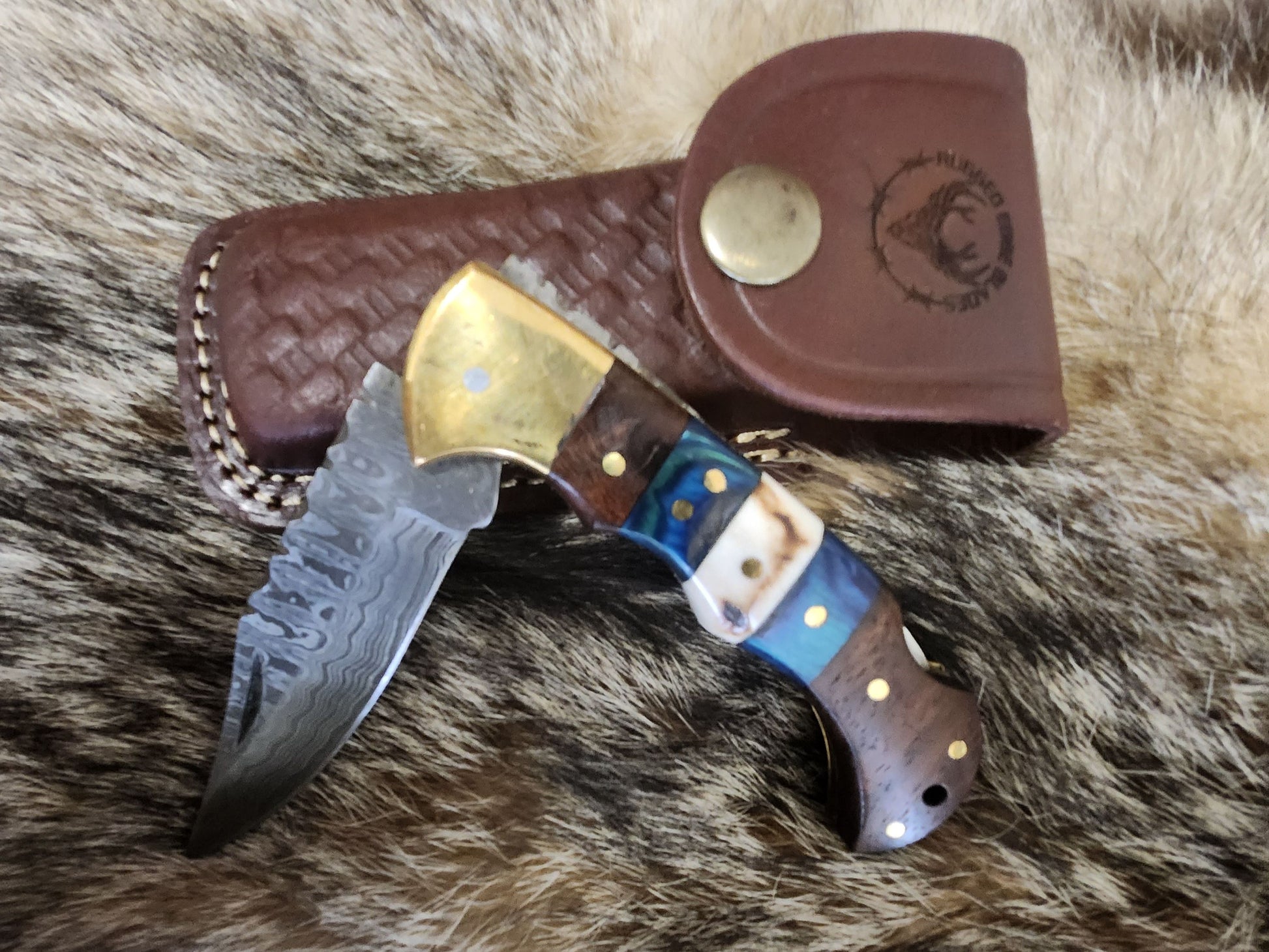 Walnut and Blue Stag pocket knife with Damascus steel blade, brass bolsters, and multicolored handle, displayed with leather sheath.