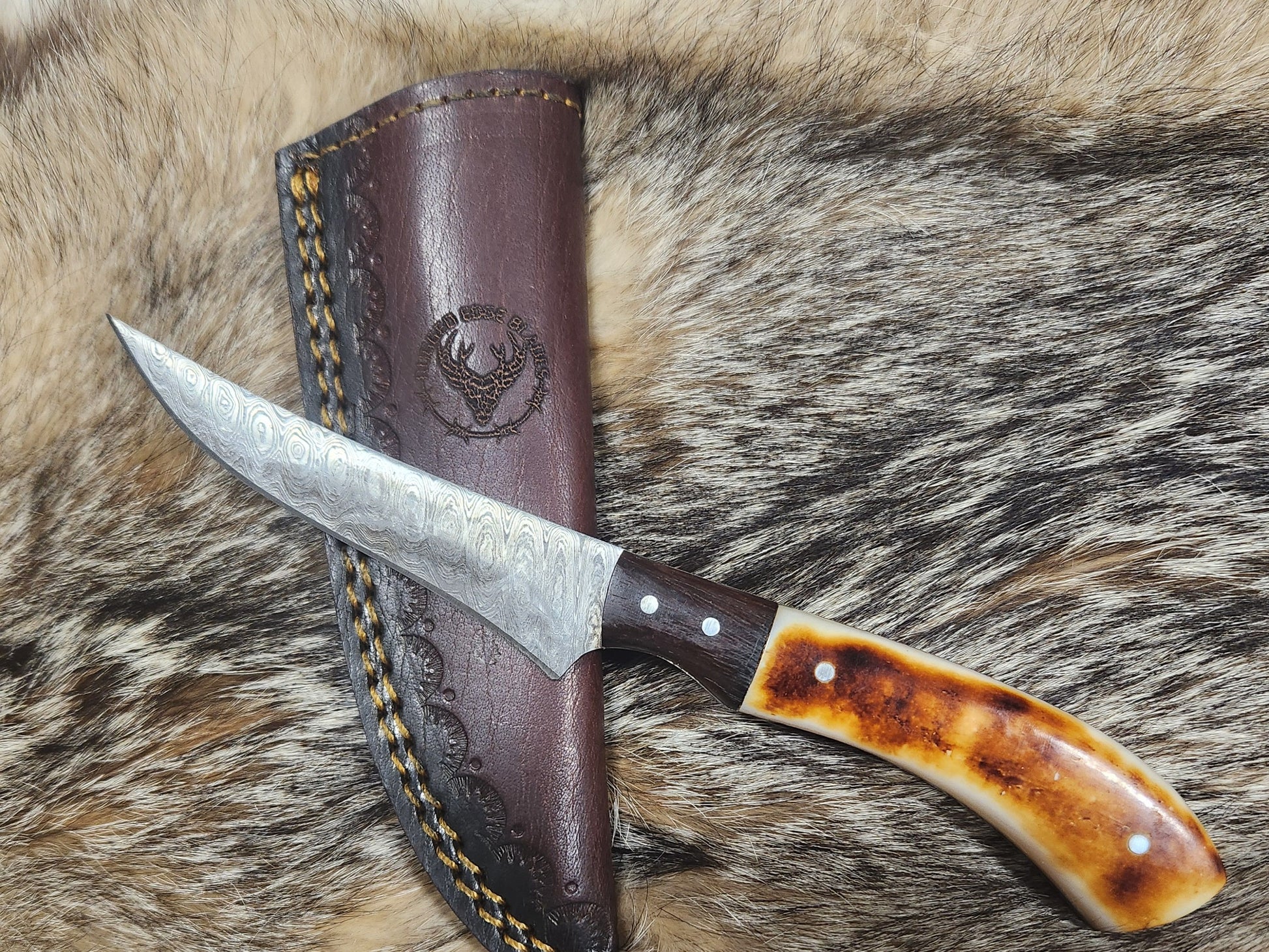 Small Bone Filet knife with Damascus steel blade and polished bone handle, displayed on fur with embossed leather sheath. Ideal for precision filleting.