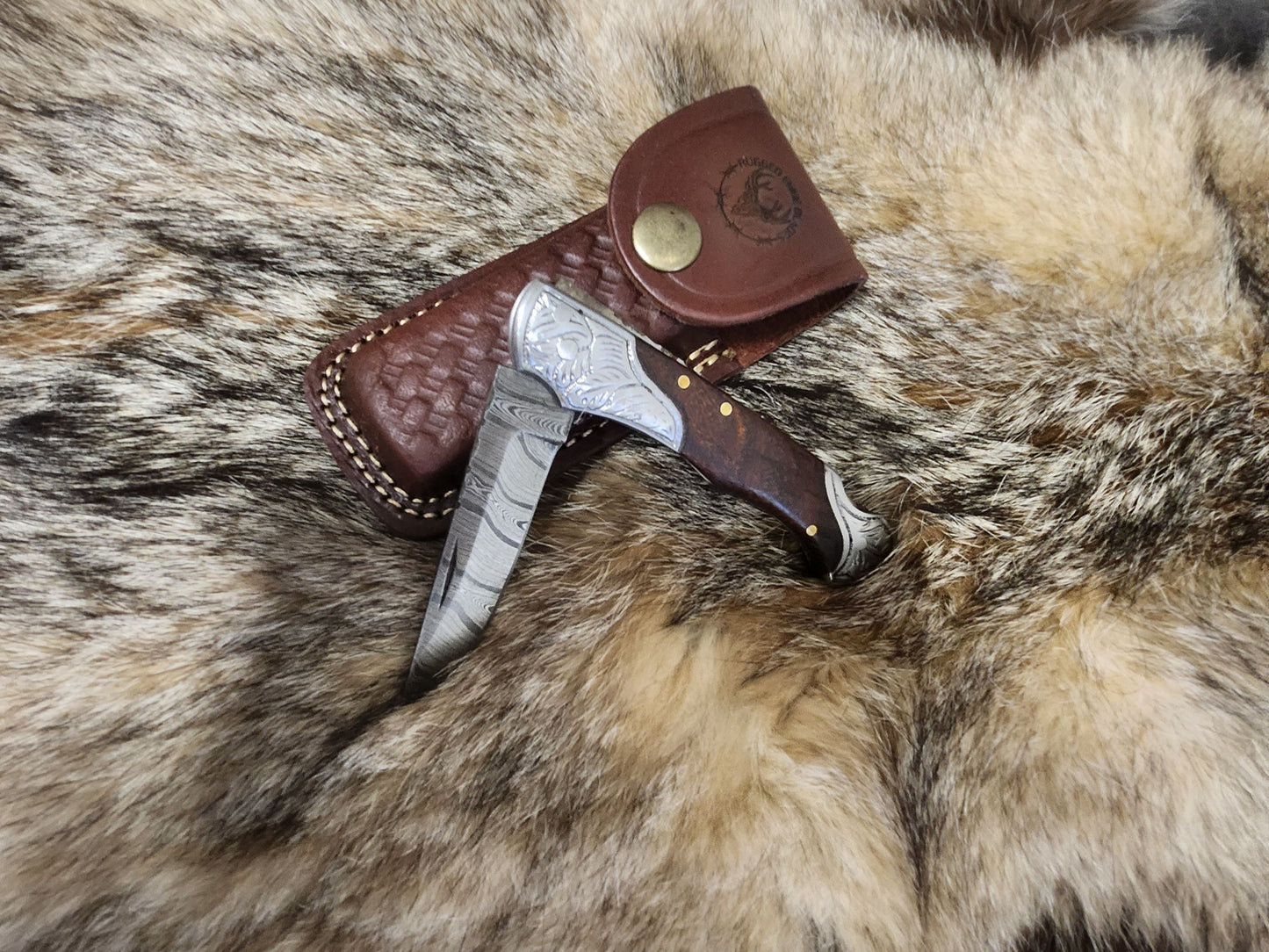 Slim Wood Folder collectible knife with engraved Damascus steel blade and polished wooden handle, displayed with leather sheath on fur background.