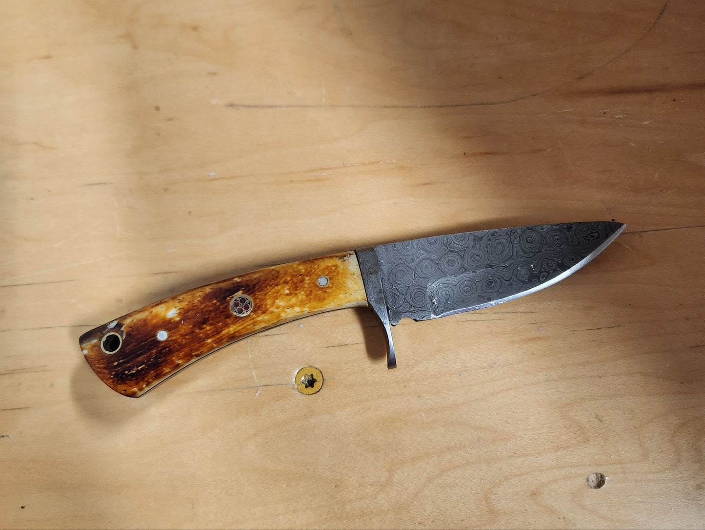 Damascus Drop Point Hunter knife with patterned steel blade and polished wood handle, ideal for camping and everyday use.