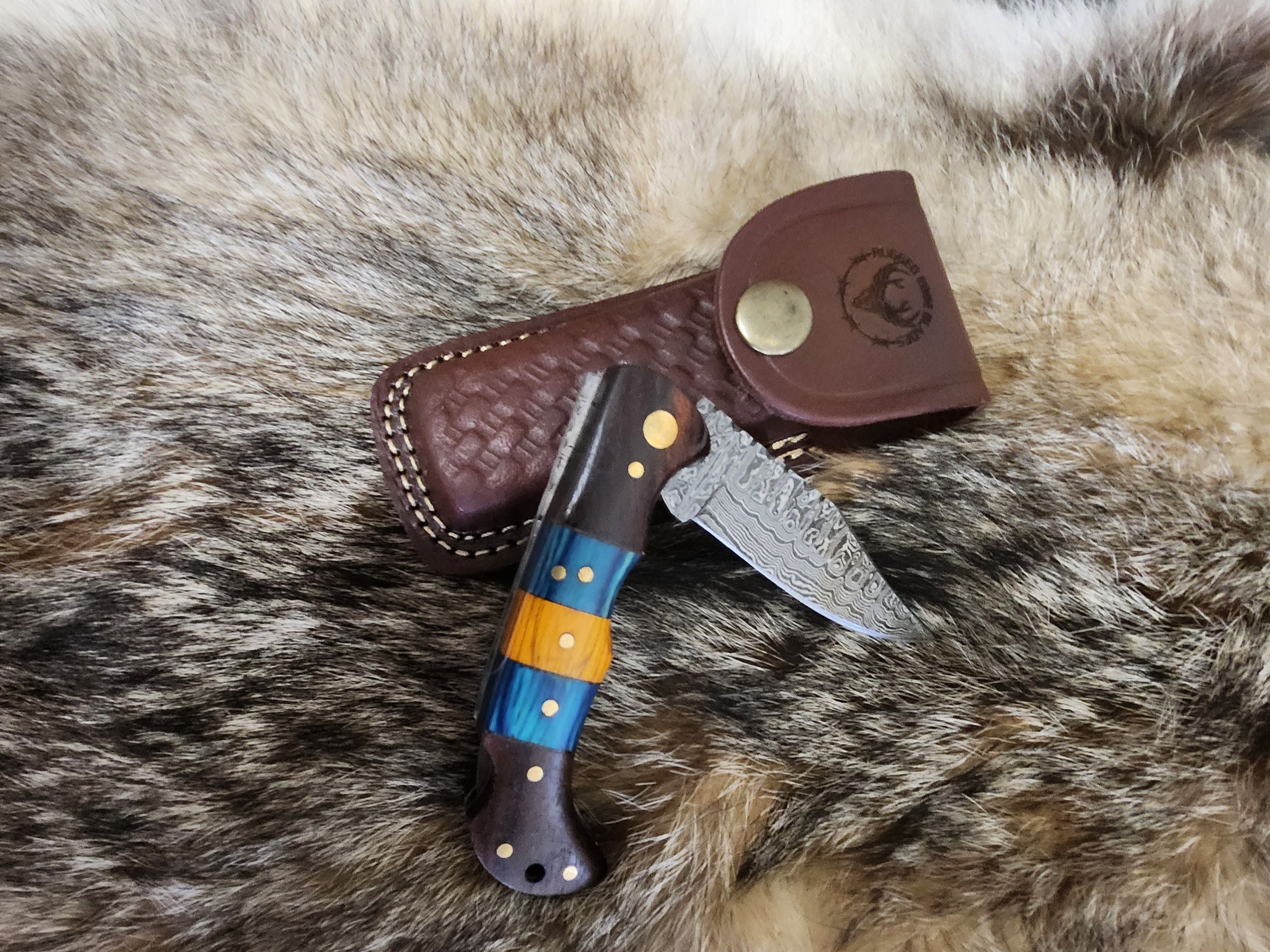Yellow and Blue Diamond Wood hunting knife with Damascus steel blade and custom handle, displayed with brown leather sheath on fur background.