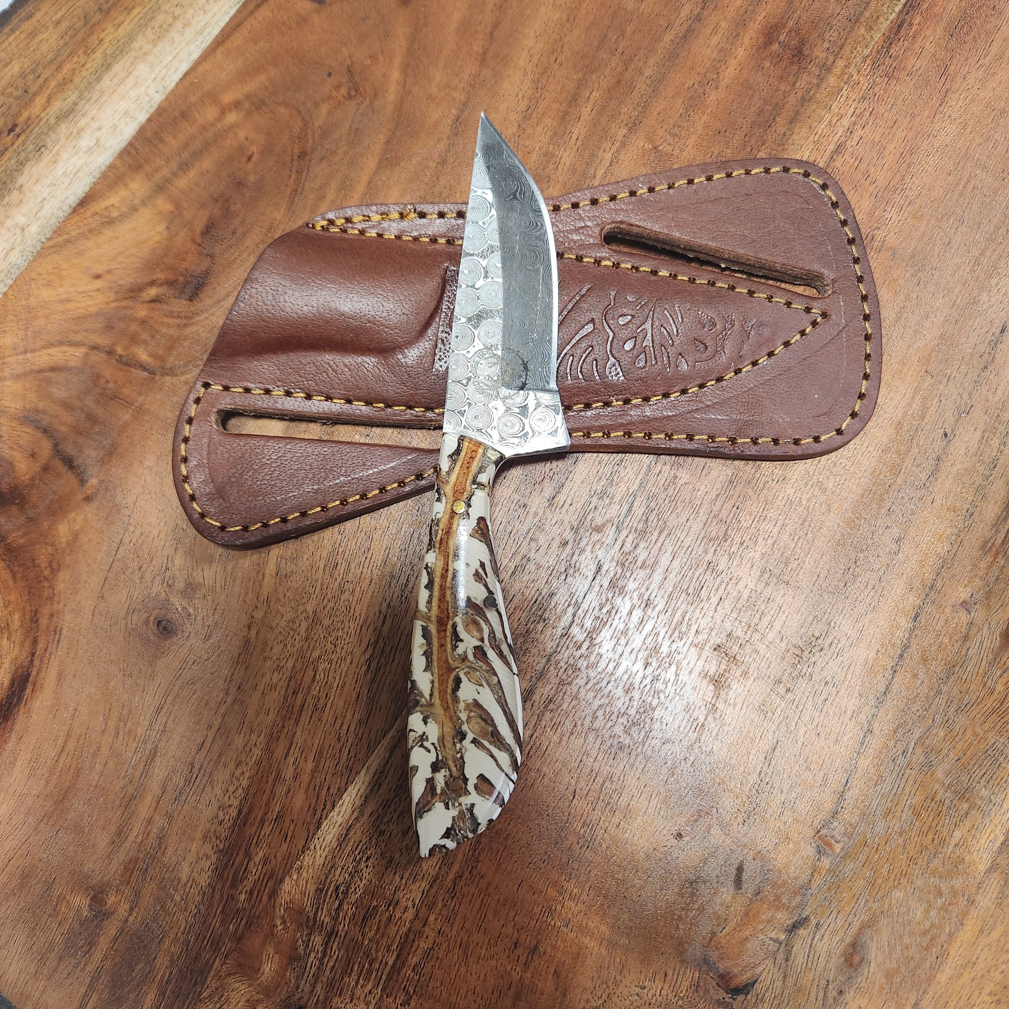 White Pinecone Wide Handle EDC knife with a patterned fixed blade and ergonomic pinecone resin handle, displayed on a brown leather sheath.