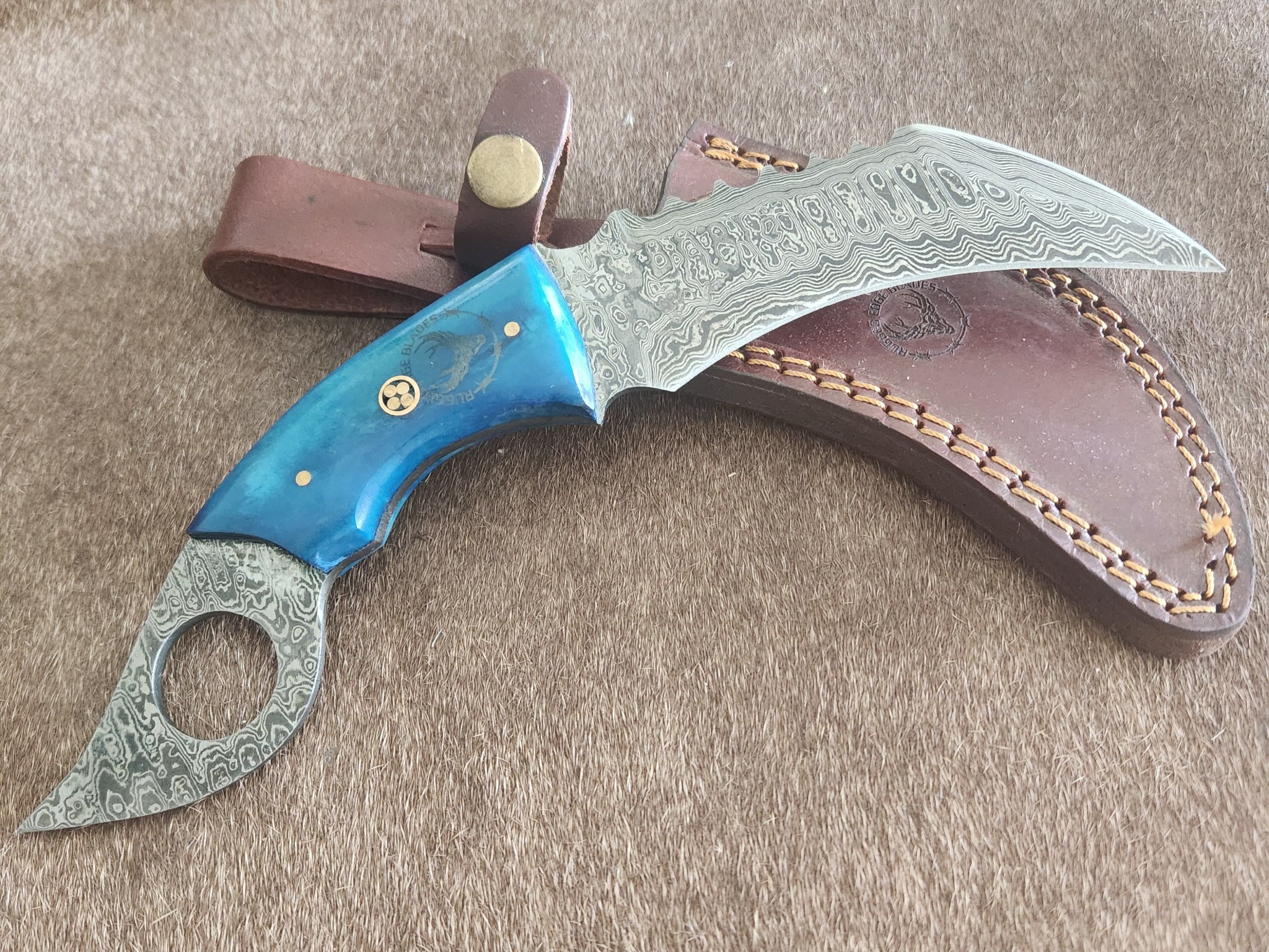 Blue Serrated Back Karambit with Damascus steel blade and ergonomic blue resin handle, displayed with brown leather sheath for tactical use.